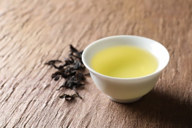 Cup of Da Hong Pao oolong and tea leaves on table, space for text