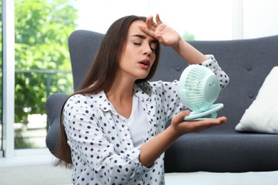 Photo of Woman with portable fan suffering from heat at home. Summer season