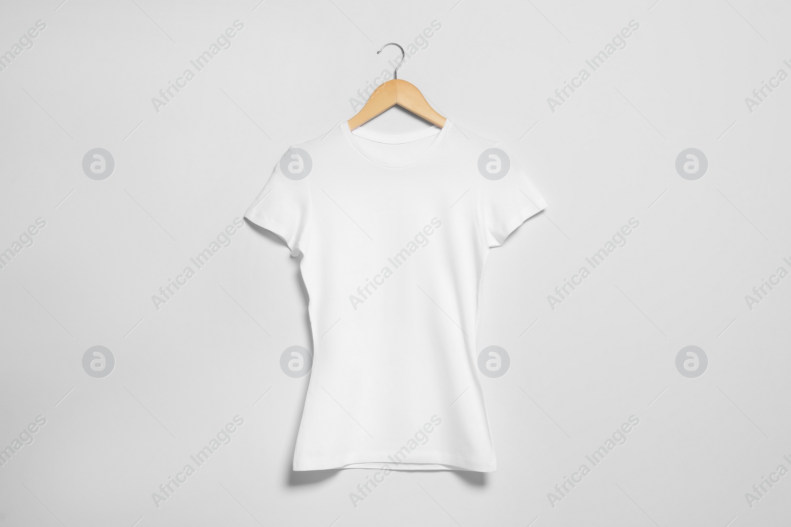 Photo of Hanger with white t-shirt on light wall. Mockup for design