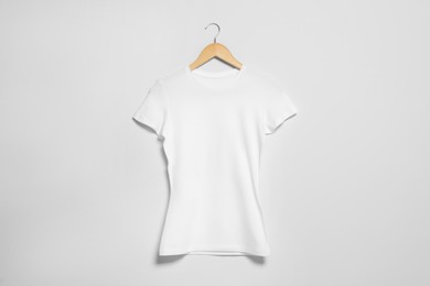 Photo of Hanger with white t-shirt on light wall. Mockup for design