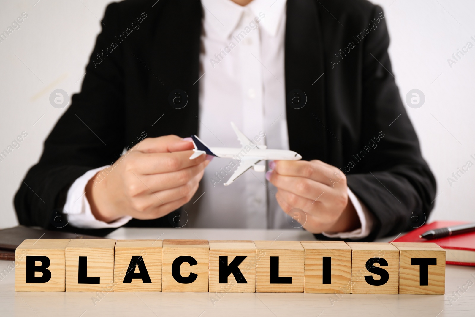 Photo of Word Blacklist of cubes and travel agent with toy airplane at white wooden table, closeup