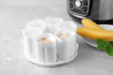 Photo of Cups of yogurt with bananas and multi cooker on table