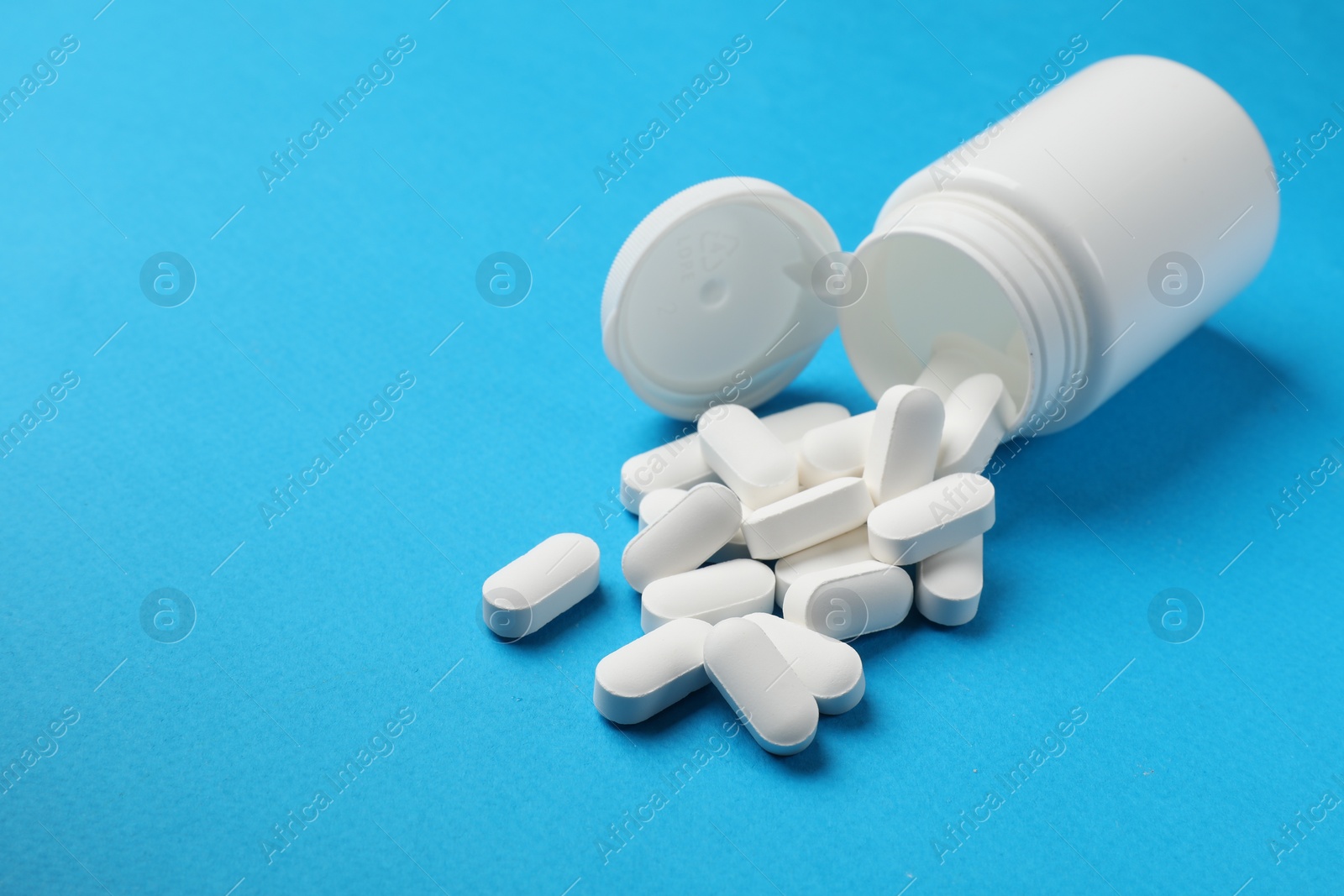 Photo of Vitamin pills and bottle on light blue background