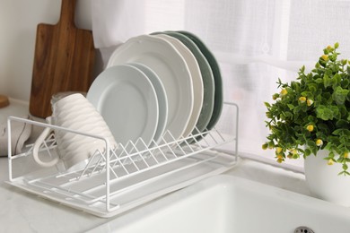 Photo of Drainer with different clean dishware, cup and houseplant on light table indoors