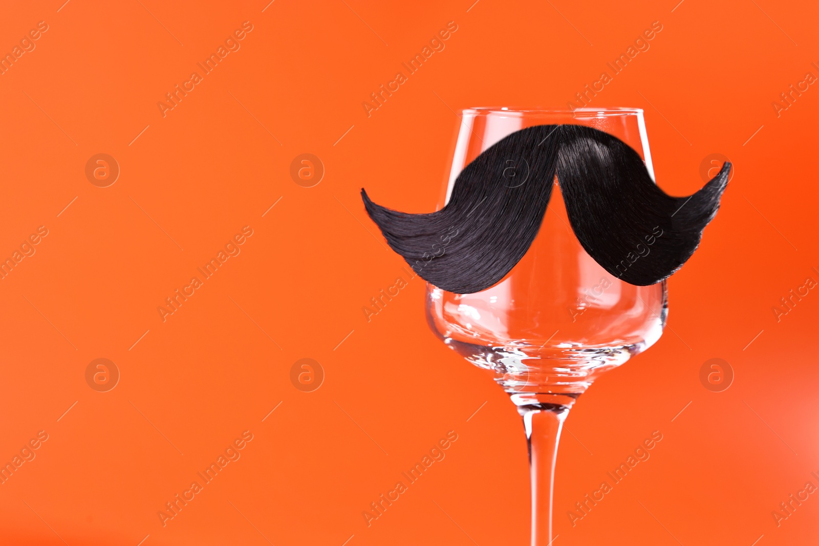 Photo of Man's face made of artificial mustache and wine glass on orange background. Space for text
