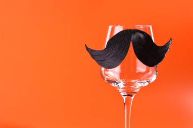 Photo of Man's face made of artificial mustache and wine glass on orange background. Space for text