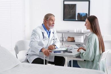 Professional orthopedist consulting patient at table in clinic