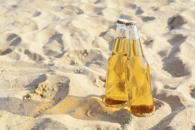 Bottles of cold beer on sandy beach. Space for text