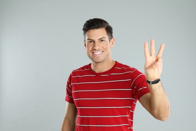 Photo of Man showing number three with his hand on grey background