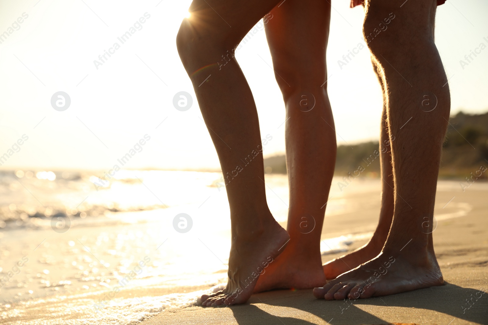 Photo of Couple on sandy beach near sea at sunset, closeup of legs