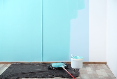 Photo of Paint roller for interior decorating with bucket on floor in room