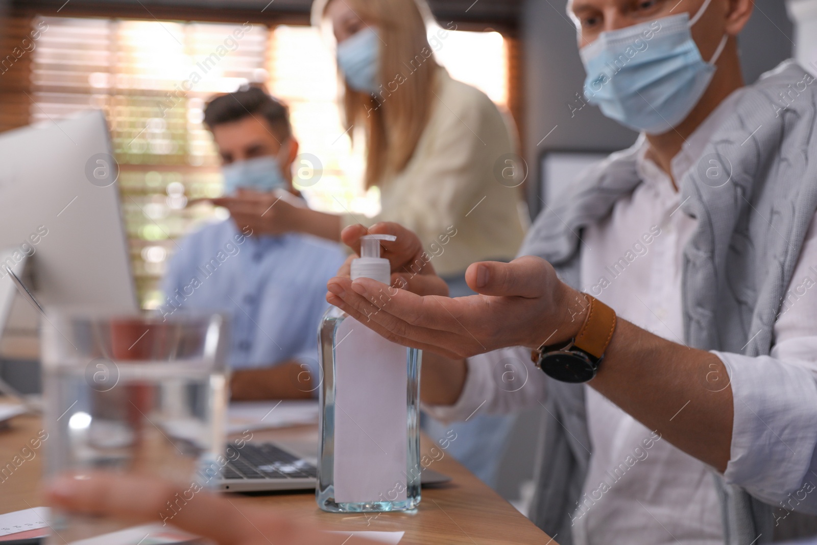 Photo of Office worker using hand sanitizer at table, closeup. Personal hygiene during COVID-19 pandemic