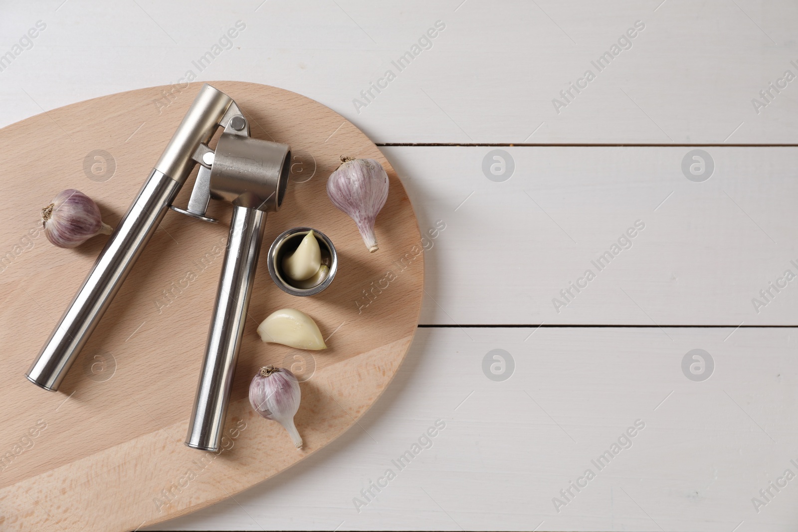 Photo of Metal press and garlic on white wooden table, top view. Space for text