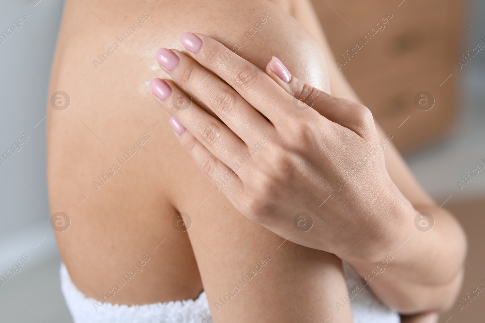 Photo of Woman applying body oil onto shoulder indoors, closeup