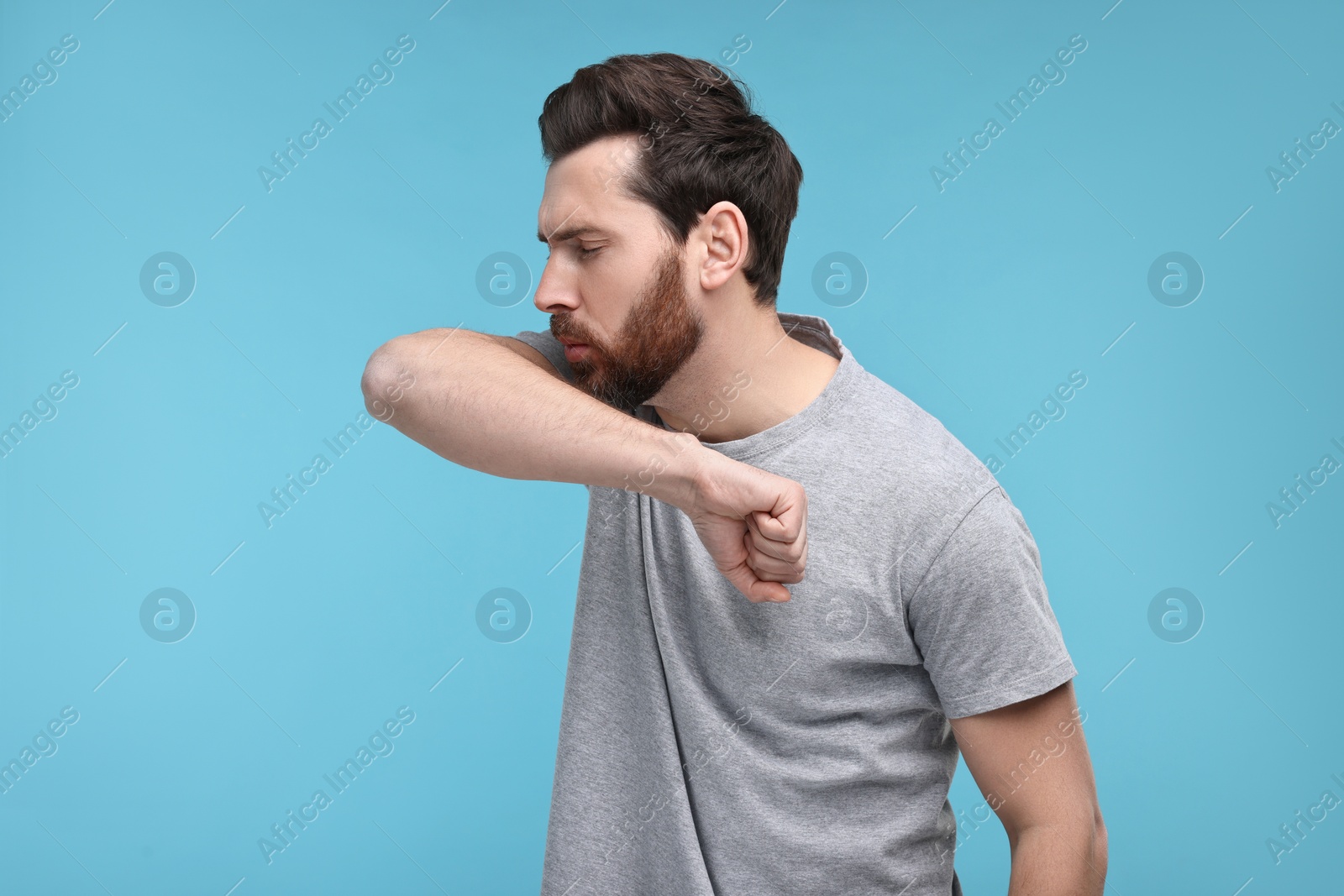 Photo of Sick man coughing into his elbow on light blue background. Cold symptoms