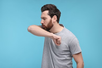 Photo of Sick man coughing into his elbow on light blue background. Cold symptoms