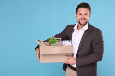 Photo of Happy unemployed man with box of personal office belongings on light blue background. Space for text