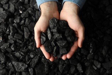 Photo of Man holding coal in hands over pile, top view