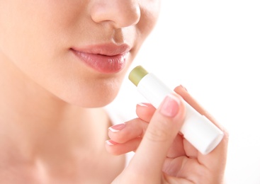 Young woman applying balm on her lips against light background, closeup