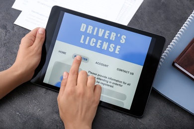 Person using tablet to fill driver's license application form at grey table, closeup