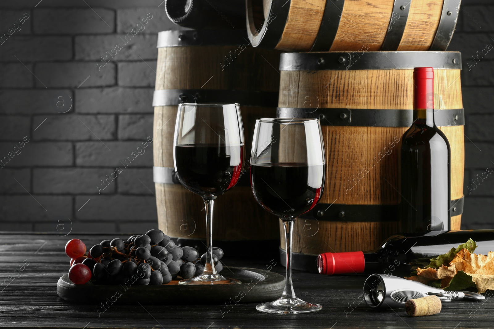 Photo of Delicious wine, wooden barrels and fresh grapes on black table