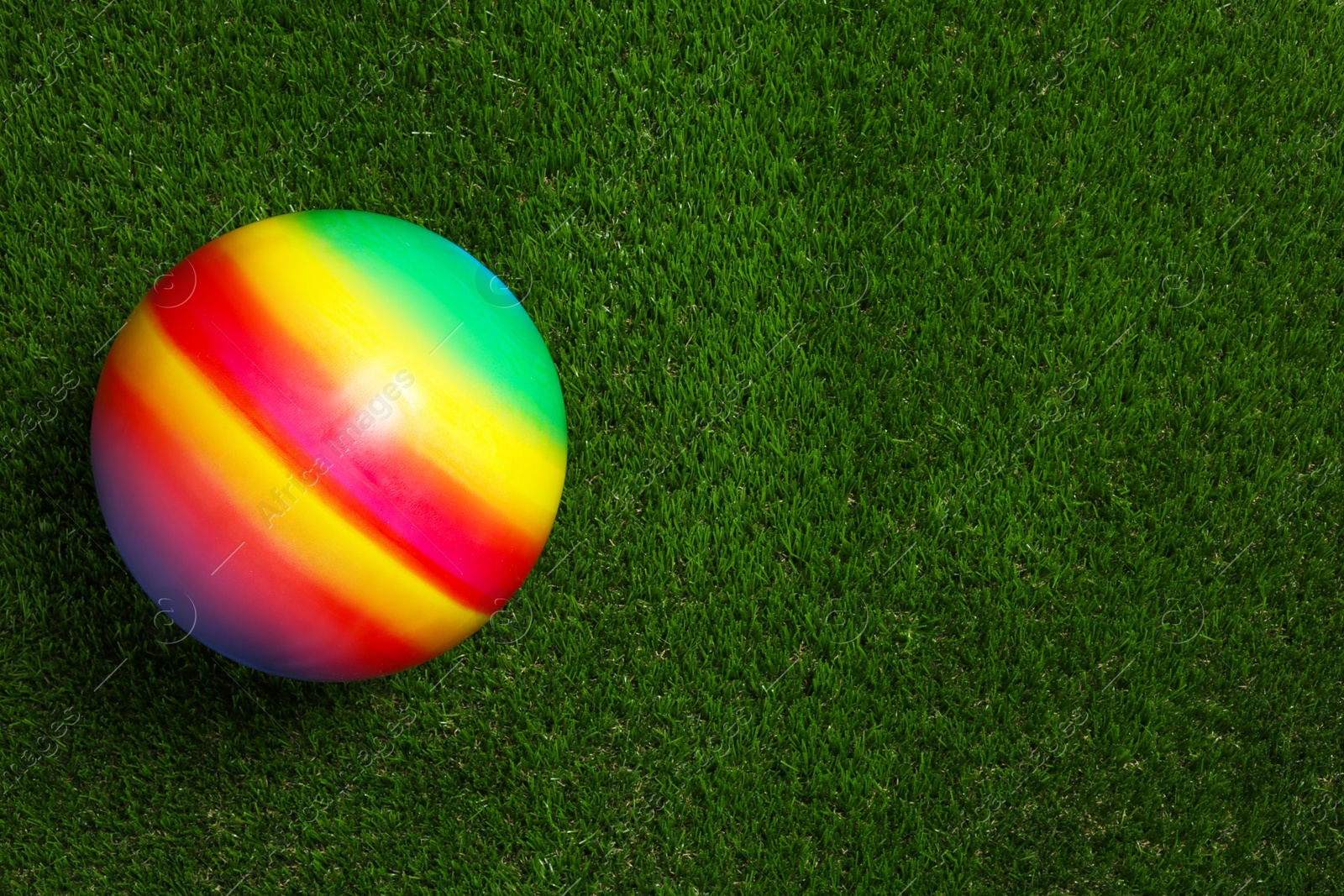 Photo of New bright kids' ball on artificial green grass, top view. Space for text