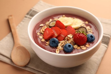 Delicious smoothie bowl with fresh berries, banana and granola on pale orange background, closeup