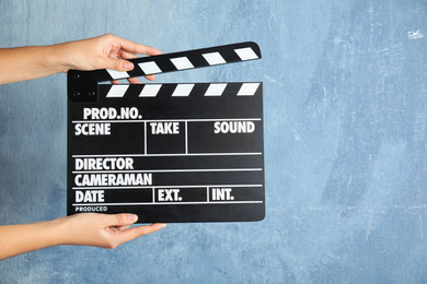 Woman holding clapperboard against color wall, closeup with space for text. Cinema production