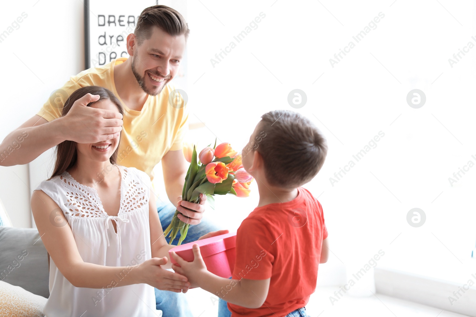 Photo of Happy woman receiving gifts from her husband and son at home. Mother's day celebration