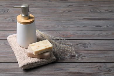 Photo of Soap bars, dispenser and terry towel on wooden table. Space for text