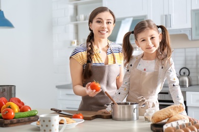 Young nanny with cute little girl cooking together in kitchen