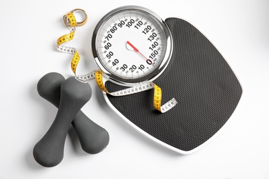 Composition with scales, tape measure and dumbbells on white background, top view