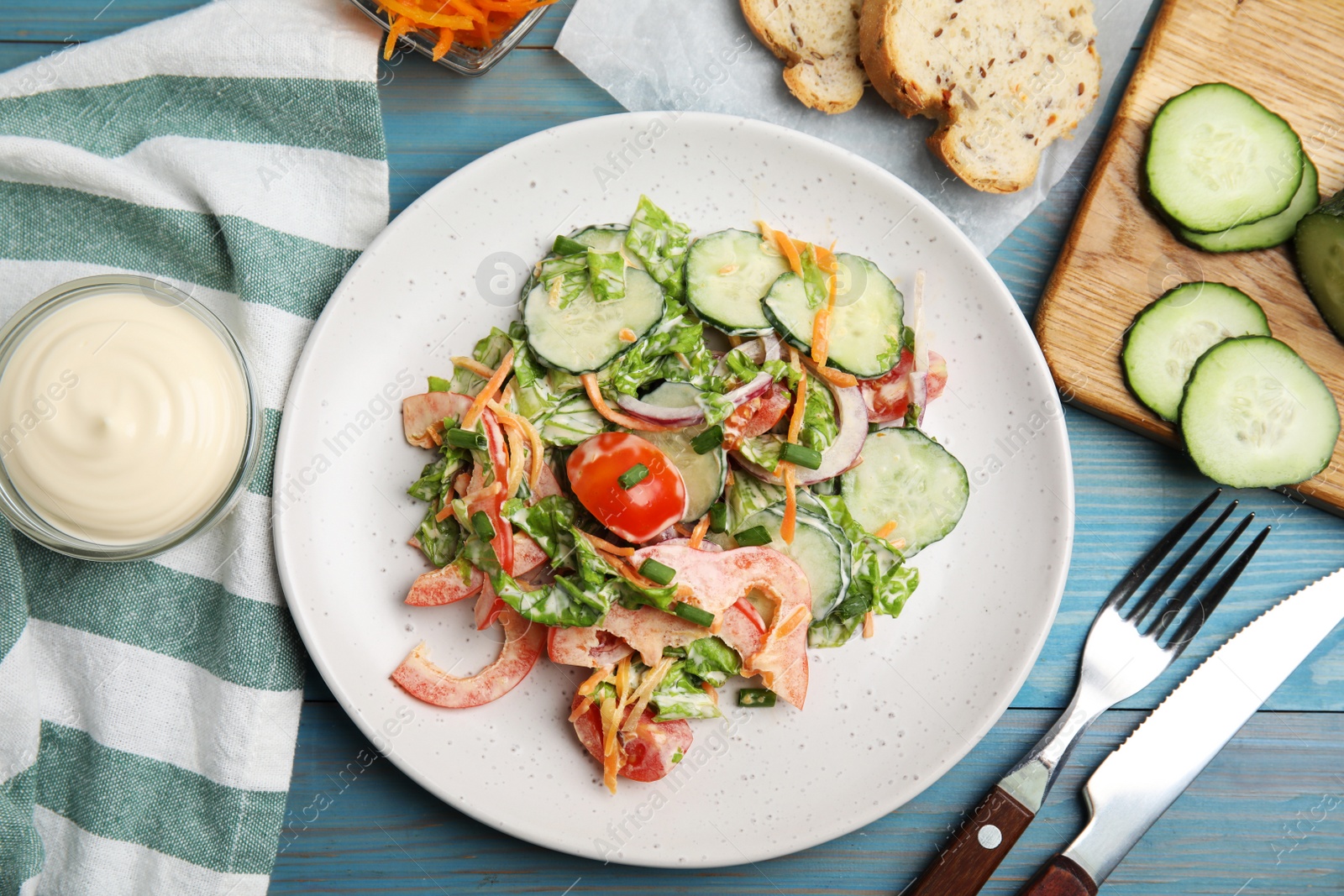 Photo of Plate of delicious vegetable salad dressed with mayonnaise served on light blue wooden table, flat lay