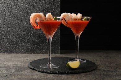 Tasty shrimp cocktail with sauce in glasses and lime on grey textured table