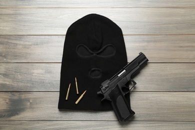 Photo of Balaclava, pistol and bullets on wooden table, flat lay