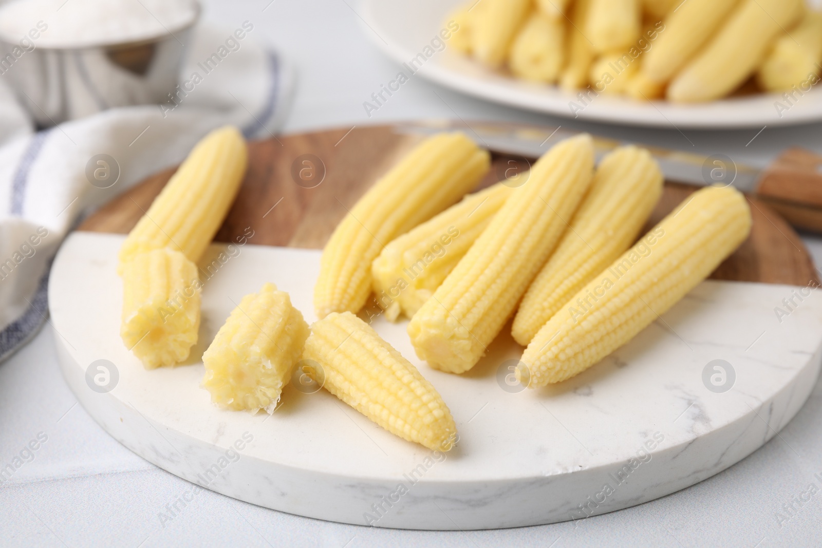 Photo of Tasty fresh yellow baby corns and knife on white tiled table, closeup