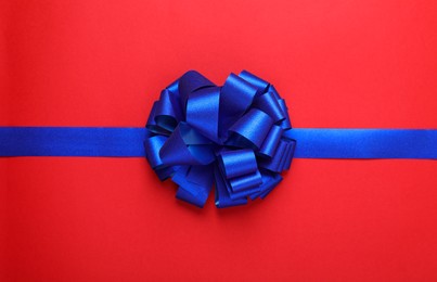 Photo of Blue ribbon with bow on red background, top view