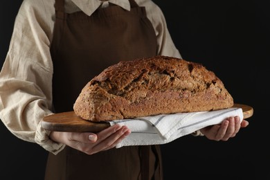 Woman holding freshly baked bread on black background, closeup