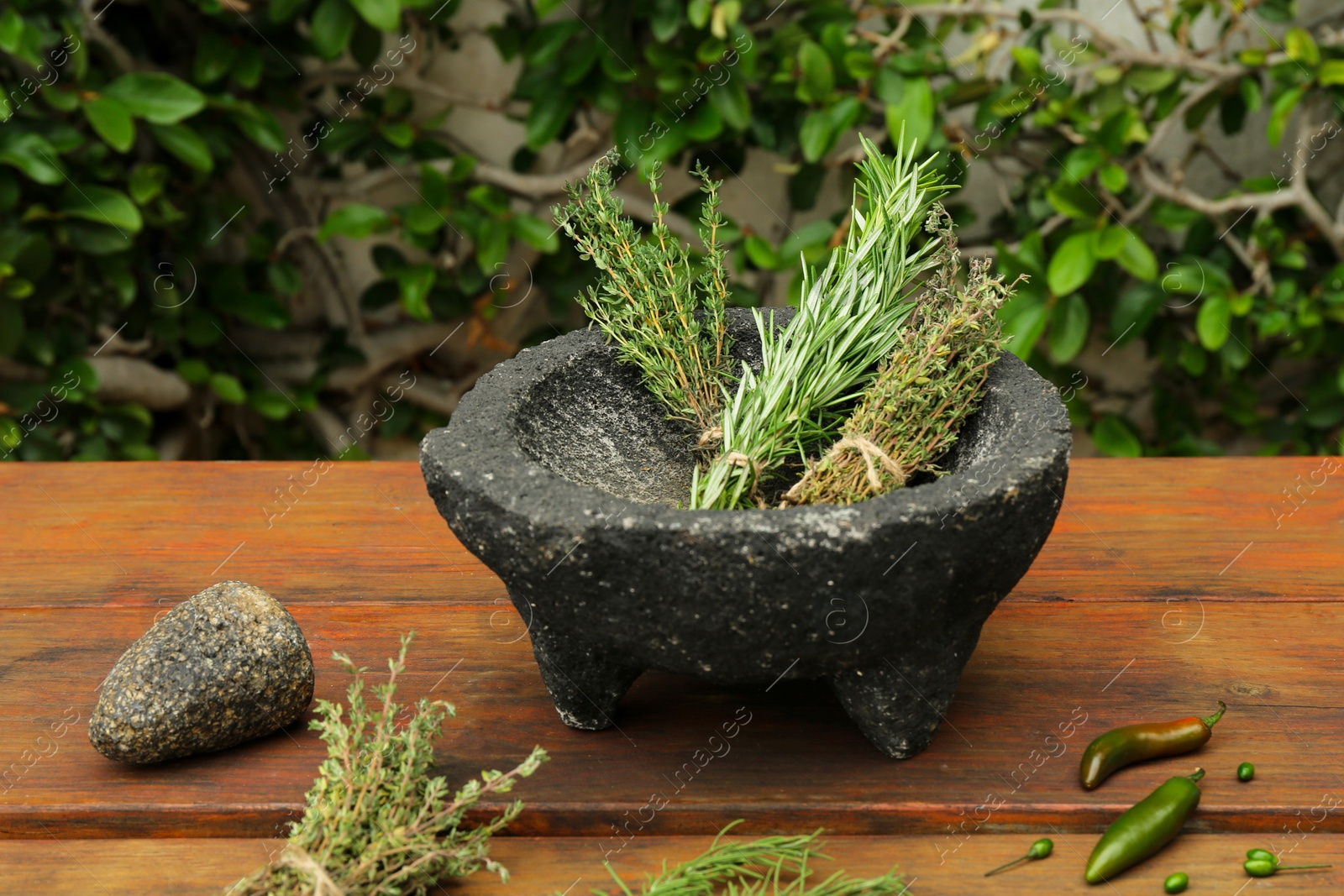 Photo of Mortar, different herbs and vegetables on wooden table outdoors