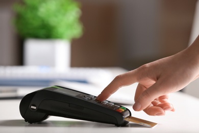 Woman using modern payment terminal at table indoors, closeup. Space for text