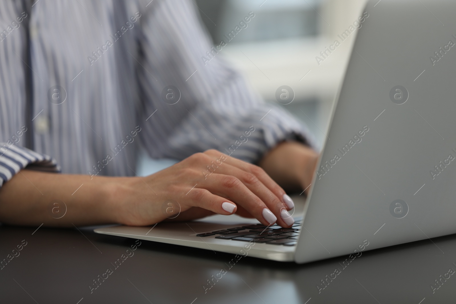 Photo of Woman using modern laptop at black desk in office, closeup