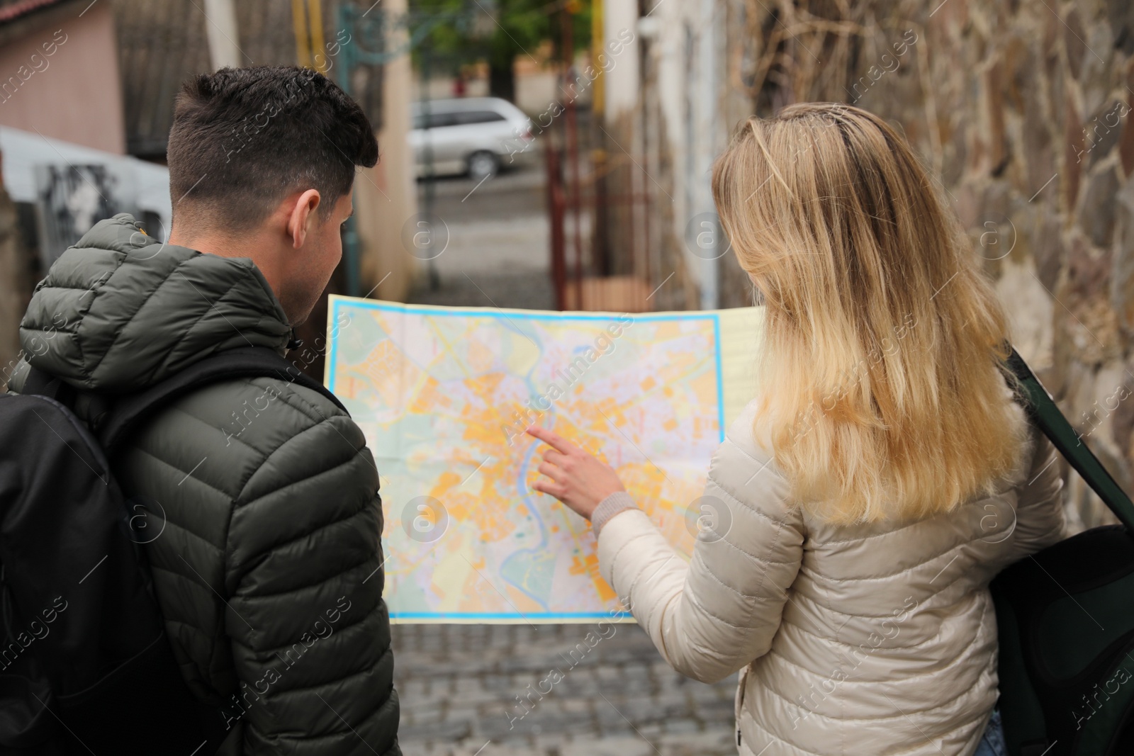 Photo of Couple of tourists with map planning trip on city street, back view