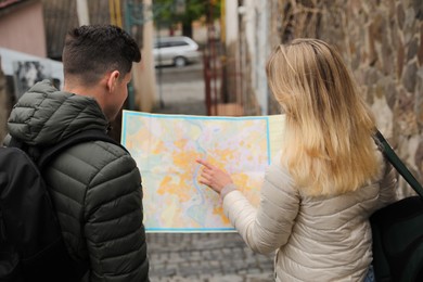 Photo of Couple of tourists with map planning trip on city street, back view