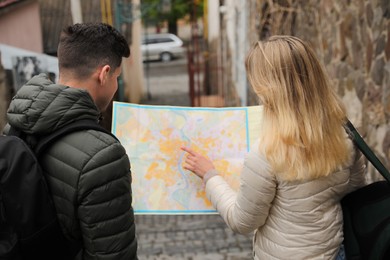 Couple of tourists with map planning trip on city street, back view