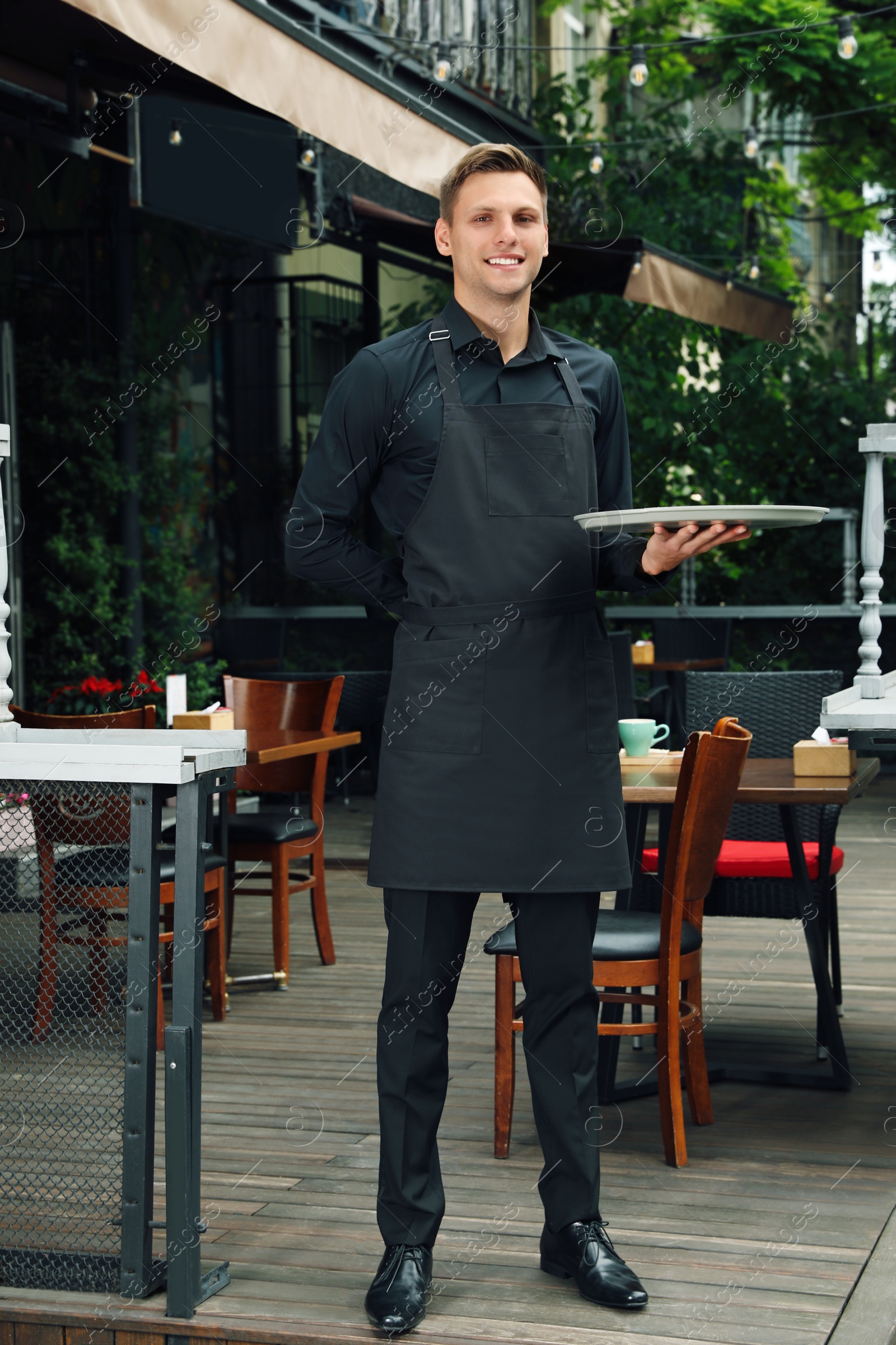 Photo of Happy young waiter with tray near cafe