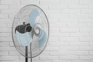 Photo of Electric fan near white brick wall, space for text. Summer heat
