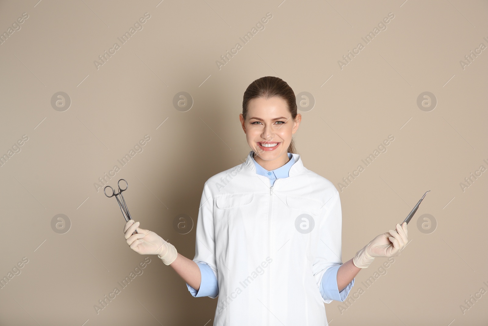 Photo of Female dentist holding professional tools on color background