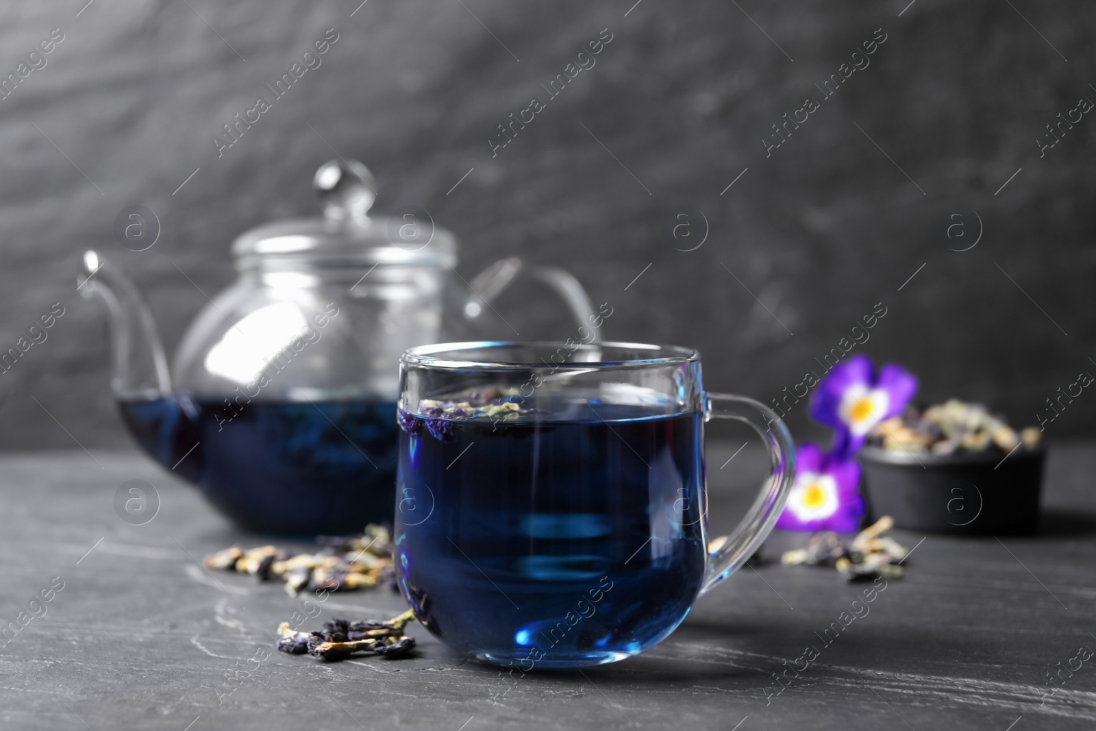 Photo of Glass cup of organic blue Anchan on black table, space for text. Herbal tea