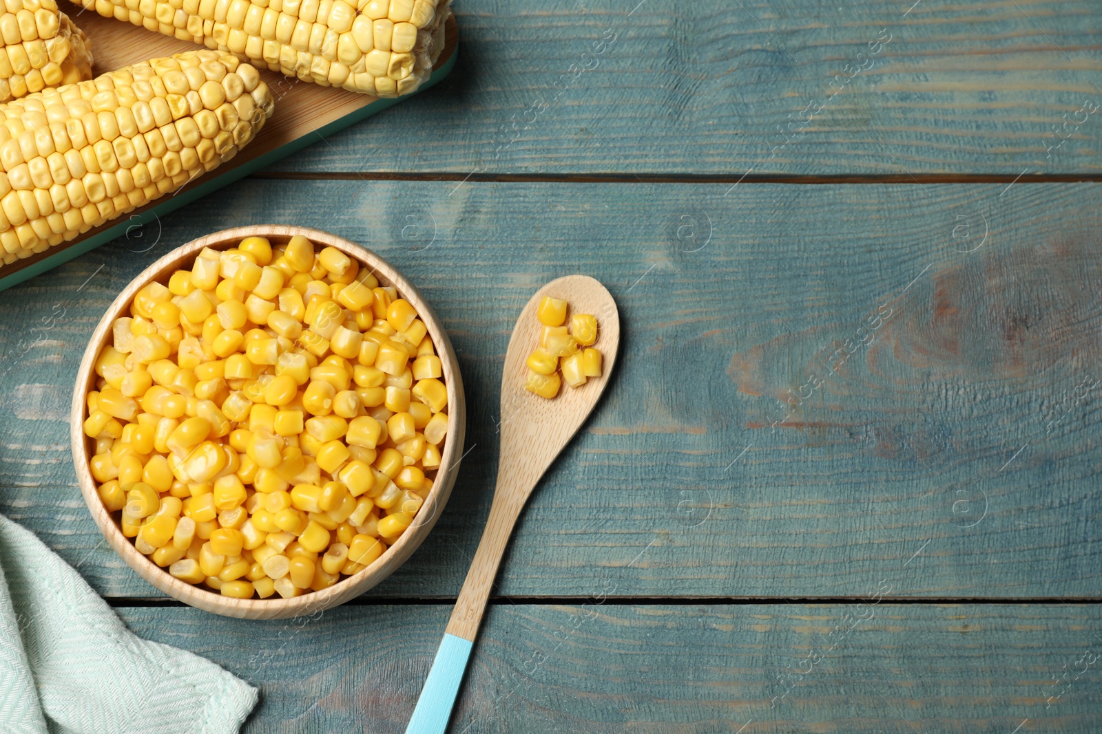 Photo of Tasty canned sweet corn on blue wooden table, flat lay. Space for text