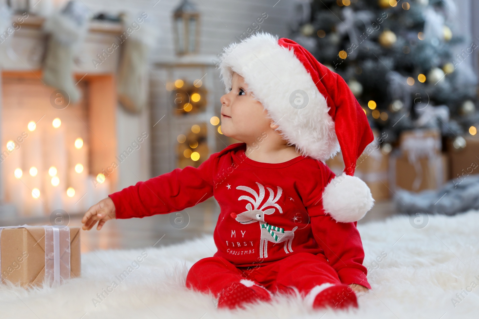 Photo of Little baby with Santa hat and Christmas gift on floor at home